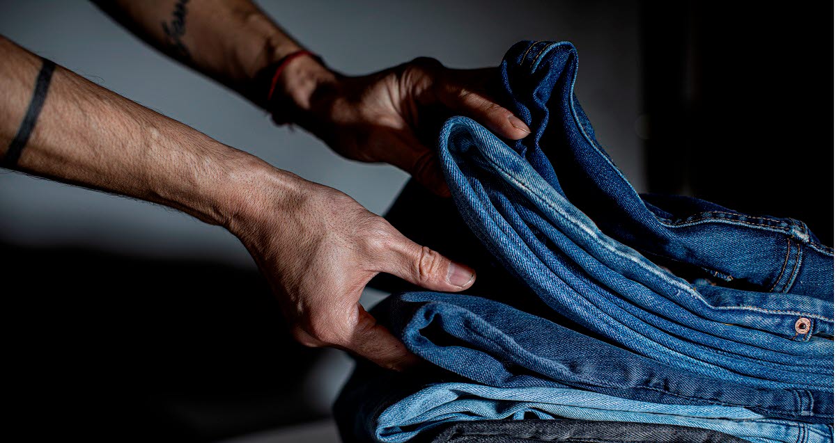 A hand holds a stack of jeans.